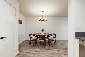 A dining area with a wooden table, six chairs, a chandelier, and a small plant on the table. - our Laid-Back Escape in the Heart of Palm Springs – Where Comfort, Sunshine (Palm Springs)