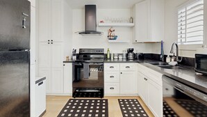 Une cuisine moderne avec des meubles blancs, un réfrigérateur noir, une cuisinière et un lave-vaisselle.