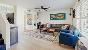 Un salon moderne avec un canapé, un fauteuil bleu, une table basse et un ventilateur de plafond.