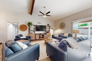 Een moderne woonkamer met leren banken, een flatscreen-televisie, houten planken en een plafondventilator.