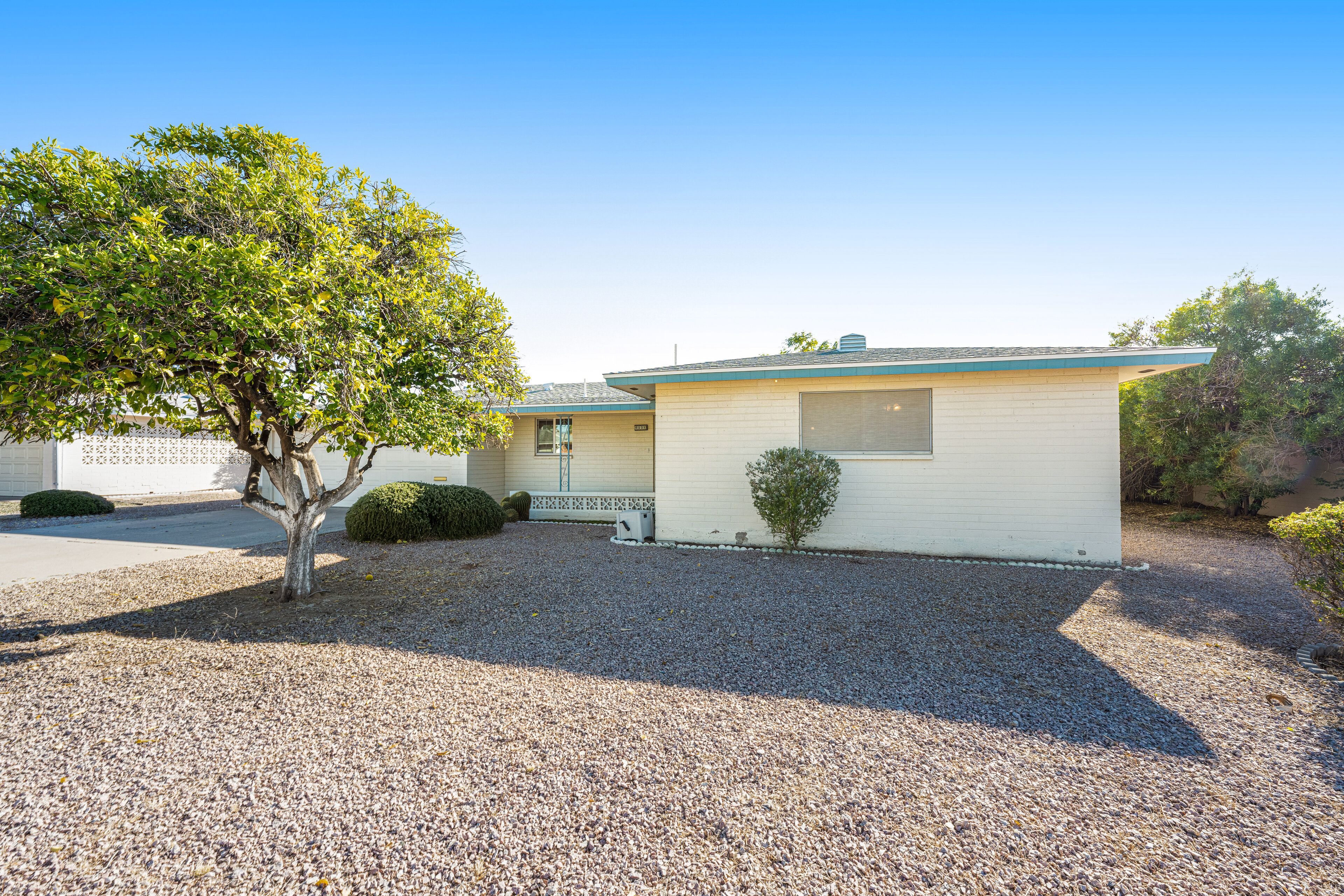 A single-story house with a gravel driveway, a small tree, and a well-maintained lawn.