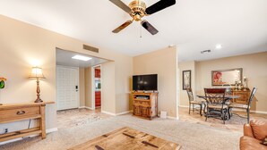 Ein geräumiges Wohnzimmer mit Couchtisch aus Holz, Deckenventilator, Fernseher und Essbereich mit Stühlen und Tisch.