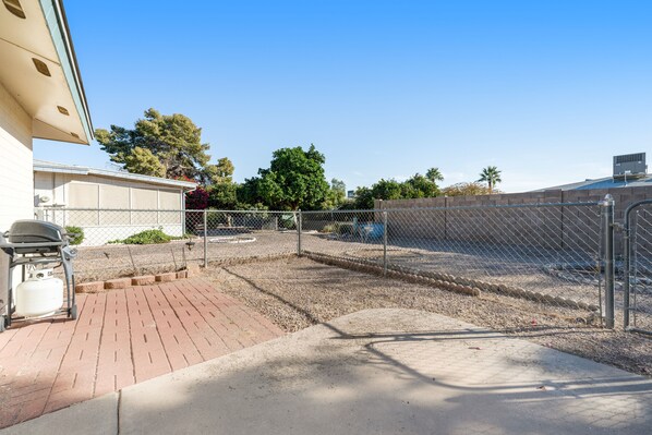 A fenced outdoor area with a gravel path, a grill, and a water tank. - Downtown Home w/Enclosed Yard, Gas Grill, Free WiFi, Central A/C, Washer/Dryer (Mesa)