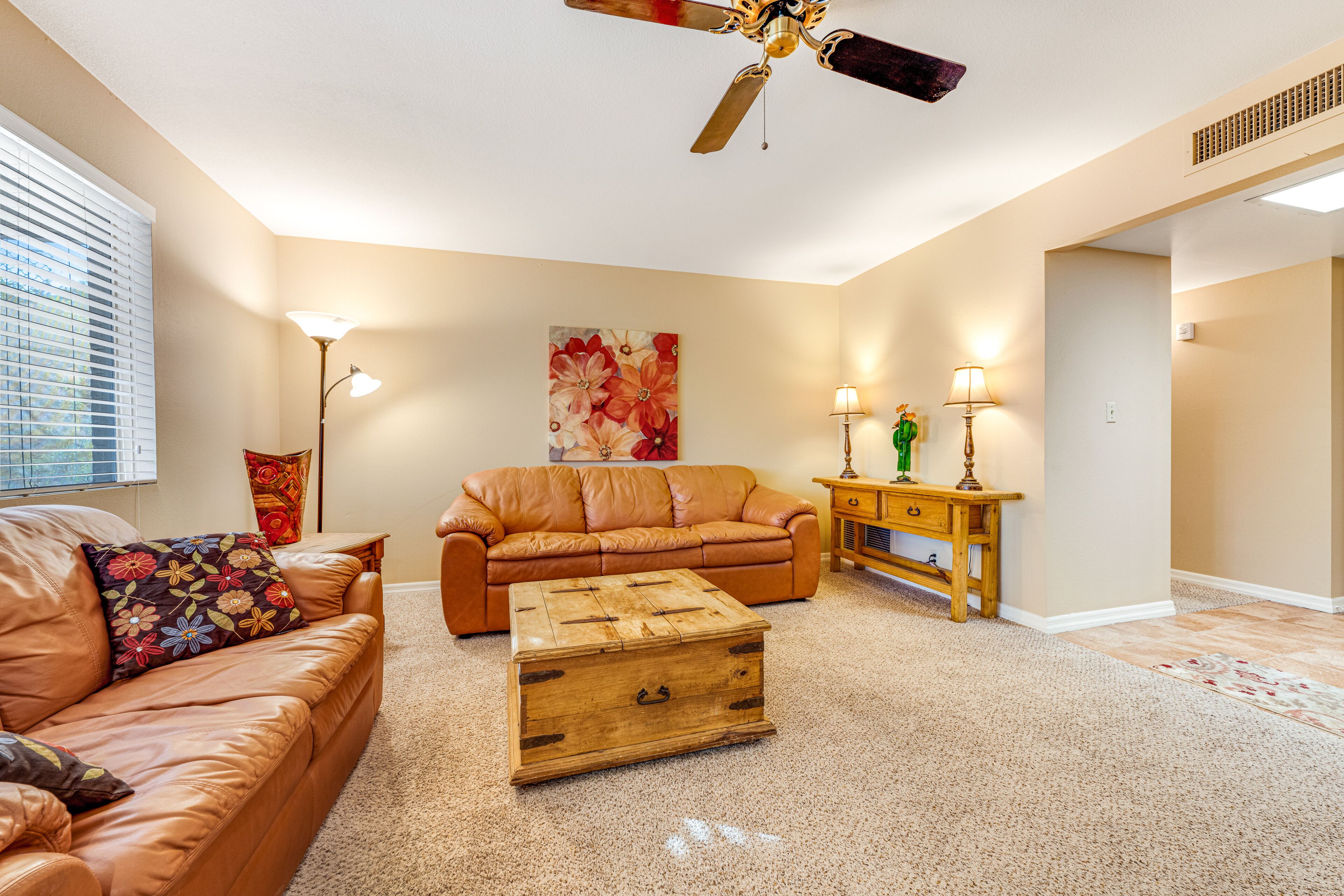 A living room with a leather sofa, a wooden chest, a floor lamp, and a ceiling fan.