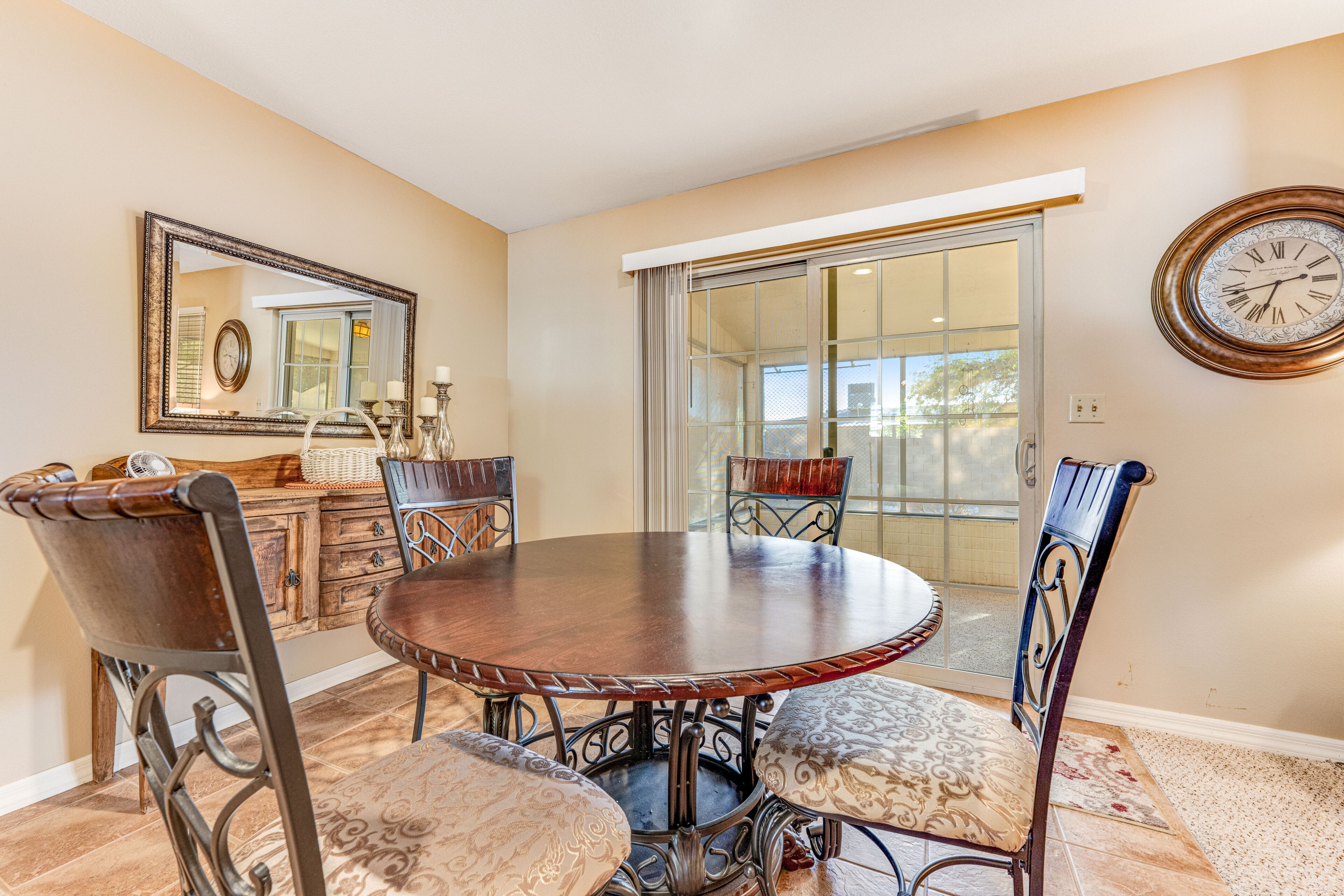 A dining area with a round table, four chairs, a mirror, and a clock on the wall.