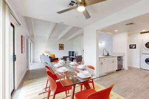 A modern kitchen with a dishwasher, a dining area with a glass table and red chairs, and a ceiling fan. - Beautiful Condo with mountain views, shared pool & pool spa (Palm Springs)