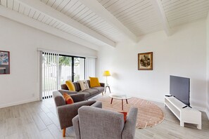 A modern living room with a sofa, armchairs, a TV, and a lamp. - Beautiful Condo with mountain views, shared pool & pool spa (Palm Springs)