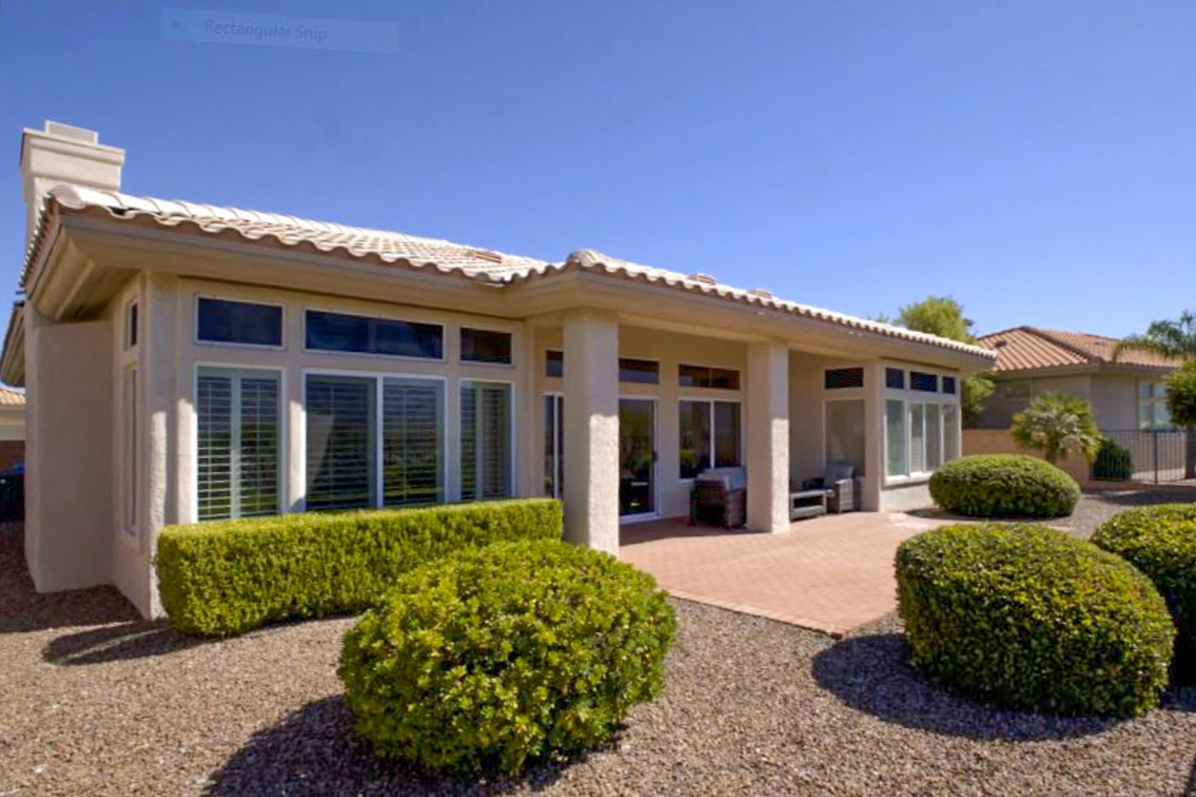 Une maison moderne dotée d’un patio couvert, de grandes fenêtres et de haies bien entretenues.