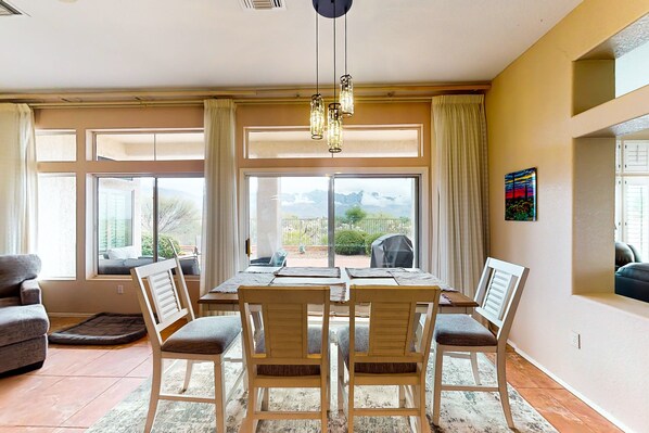 Un comedor con mesa y sillas, ventanas amplias con cortinas y vistas al exterior.