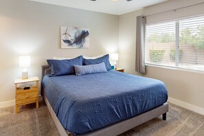 Ein Schlafzimmer mit einem großen Bett, zwei Nachttischen, einem Wandbild und einem Fenster mit Jalousien.