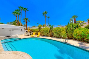 A swimming pool with clear blue water, surrounded by palm trees and a white building with a covered area. - Bright, Family-Friendly Home with Private Firepit, Heated Outdoor Pool, Pool Spa (Palm Springs)