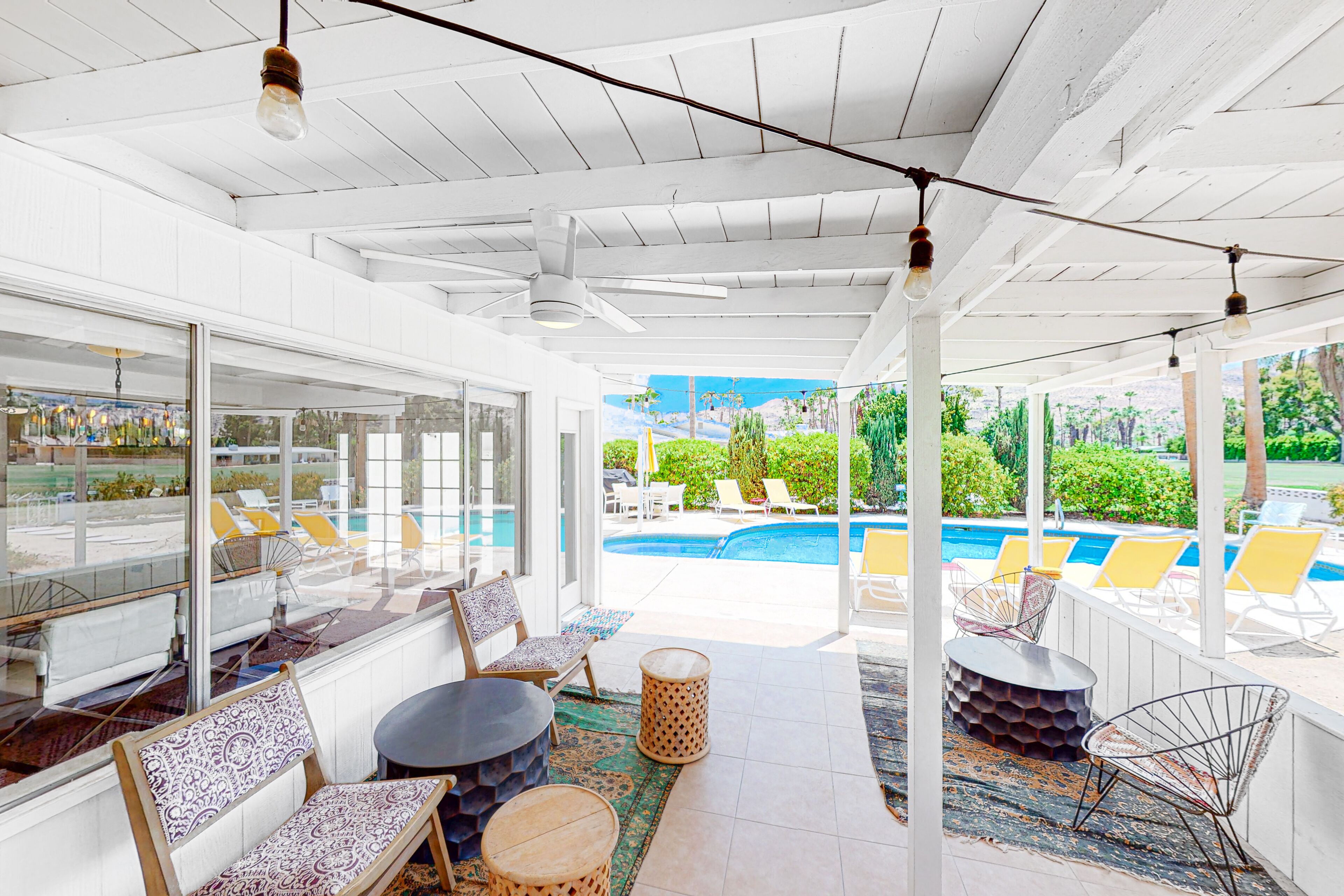 A sunlit patio area with a pool view, furnished seating, and a ceiling fan.