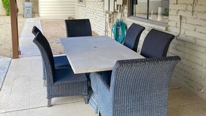 A patio with a table and chairs, a brick wall, and a window. - Sunlit & spacious desert villa with patio, games, & fire pit - near golf & parks (Paradise Valley)