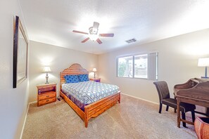 A bedroom with a bed, two bedside tables, a desk, a chair, a ceiling fan, and a window.