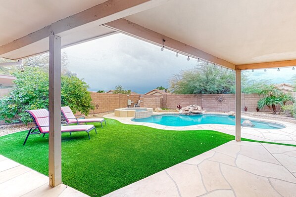 A backyard with a swimming pool, artificial grass, and patio furniture.