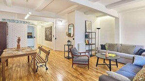 A spacious living area with a wooden dining table, a grey sofa, and a wooden bench. - AN AUTHENTIC PARISIAN STAY IN THE MOST LOVED NEIGHBOURHOOD  - RUE DU FOUR (Paris)