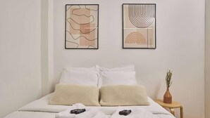 A neatly made bed with white linens and two beige textured pillows, a small wooden side table with a vase of dried plants, and two abstract paintings on the wall. - AN AUTHENTIC PARISIAN STAY IN THE MOST LOVED NEIGHBOURHOOD  - RUE DU FOUR (Paris)
