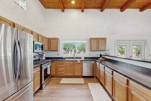 A modern kitchen with wooden cabinets, stainless steel appliances, and a large window providing a view of trees. - Modern adobe home with a community pool, washer/dryer - snowbirds welcome! (Tucson)