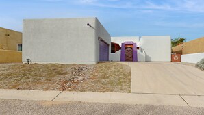 Un edificio moderno con techo plano, un camino de hormigón y un pequeño espacio con césped y rocas.