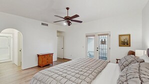 Un dormitorio con una cama grande, un ventilador de techo, un aparador de madera y una puerta que da a un balcón.