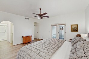 A bedroom with a large bed, a ceiling fan, a wooden dresser, and a door leading to a balcony. - Modern adobe home with a community pool, washer/dryer - snowbirds welcome! (Tucson)