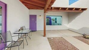 Un patio con una mesa y sillas, una puerta morada y una ventana con vista a un edificio azul.