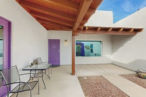 Une terrasse avec une table et des chaises, une porte violette et une fenêtre donnant sur un immeuble bleu.