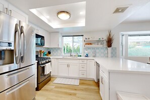 A modern kitchen with stainless steel appliances, white cabinetry, and a large window providing natural light. - Views, tranquility, private pool and spa, outdoor kitchen (Palm Springs)