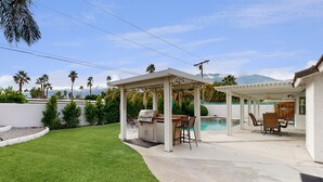 Ein Garten mit Barbereich, Sitzgelegenheiten im Freien und einem Swimmingpool.