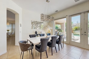 A dining area with a white table, black chairs, a chandelier, and a decorative mirror. - Oasis-style, dog-friendly home w/ a furnished patio, yard, private pool, & spa (Rancho Mirage)