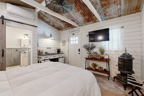 A bedroom with a large bed, a farmhouse sign, a vintage stove, and a television on the wall. - Opulent vineyard villa with private hot tub & guest suite (Temecula)