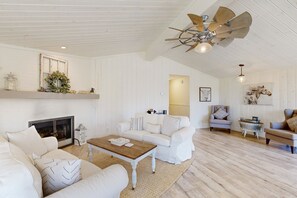 A spacious living room with a fireplace, white furniture, and a ceiling fan.