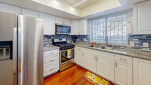 Een moderne keuken met witte kastjes, roestvrijstalen apparatuur, een magnetron, een fornuis en een raam met zonwering.