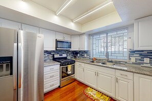 A modern kitchen with white cabinetry, stainless steel appliances, a microwave, a stove, and a window with blinds. - Centrally located retreat with pool, Ping-Pong, balcony, full kitchen, W/D, & AC (Tempe)