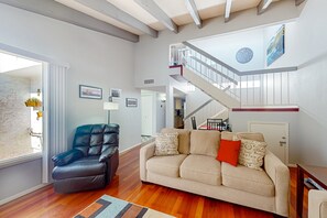 A spacious living area with a leather armchair, a beige sofa with patterned cushions, a wooden floor, a staircase with a railing, and a wall clock. - Centrally located retreat with pool, Ping-Pong, balcony, full kitchen, W/D, & AC (Tempe)