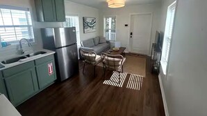 A compact kitchen with a built-in fridge, a dining area with chairs, and a sofa. - The Pass Picture Book (Pass Christian)