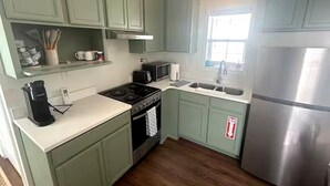 A kitchen with green cabinets, a stainless steel refrigerator, a microwave, a stove, and a sink. - The Pass Picture Book (Pass Christian)