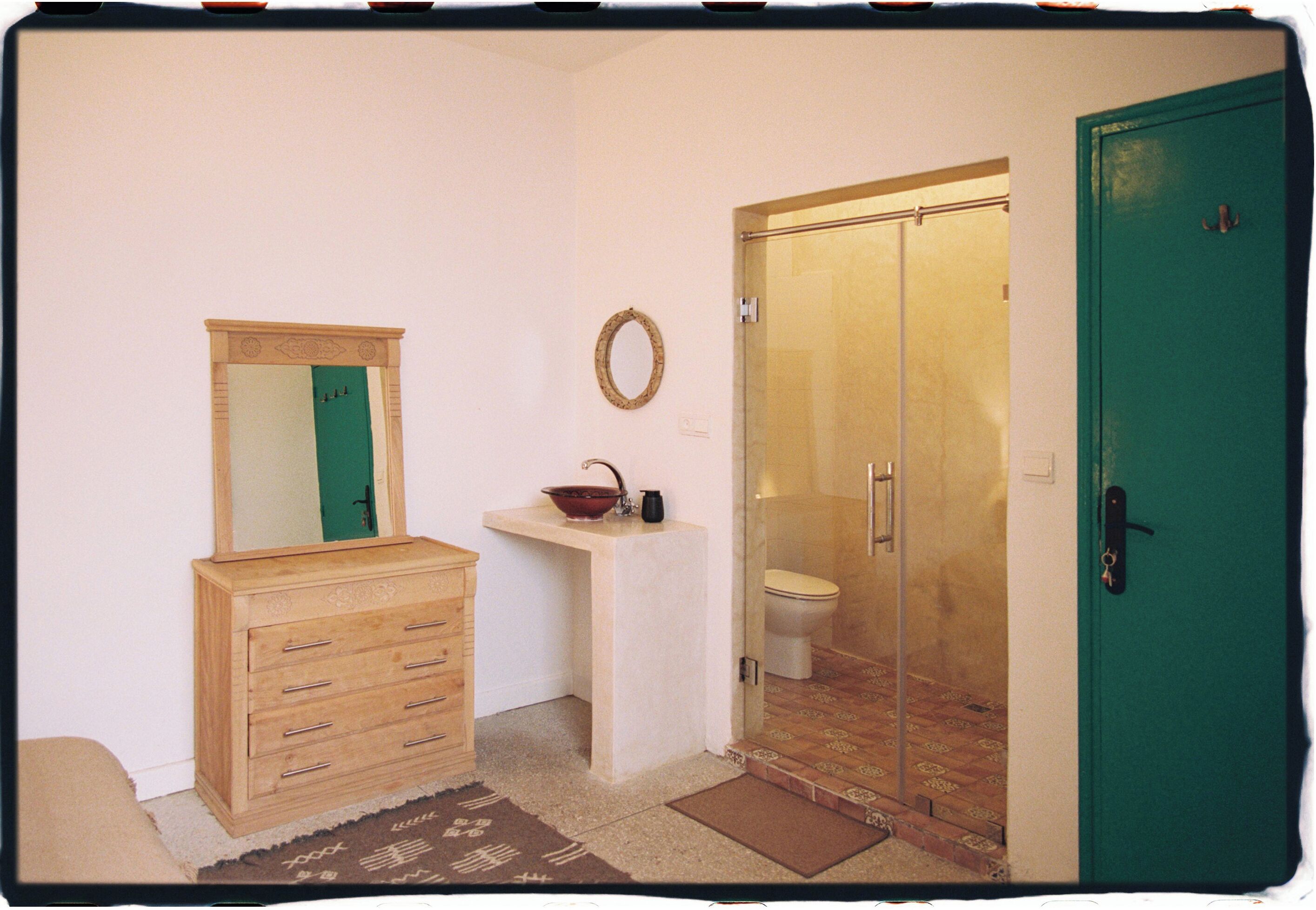 Ein Badezimmer mit einem Holzbadezimmer-Möbel, einem Waschbecken, einem Spiegel, einer Duschkabine und einer grünen Tür.