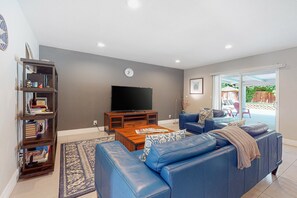 A living room with a blue sofa, a coffee table, a TV, and a bookshelf. - Dreamy, dog-friendly home w/ private pool, spa & terrace - near El Paseo (Palm Desert)