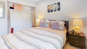 Une chambre à coucher bien rangée, avec un lit, des lampes de chevet, une table de chevet et des œuvres d’art accrochées au mur.
