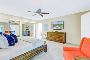A bedroom with a bed, a ceiling fan, a TV, a wooden dresser, and a bright orange chair. - Racquet Club East Home with Modern Flair | Pool, Spa & Outdoor Living (Palm Springs)