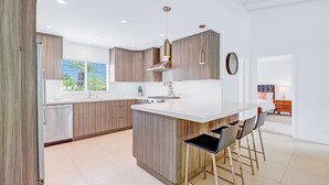 Een moderne keuken met een centraal eiland, barkrukken en uitzicht op het buiten.