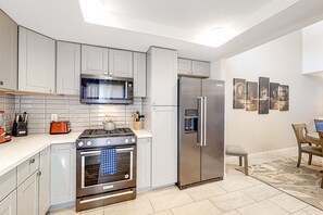A modern kitchen with stainless steel appliances, grey cabinetry, and a tiled backsplash. - Dreamy Desert Hideaway | Pool, Hot Tub & 2 Patios - Near Dining, Shops & Golf (Palm Desert)