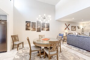 Ein modernes Wohnzimmer mit einem Esstisch aus Glas, Holzsesseln, einem blauen Sofa und einer Pendelleuchte.