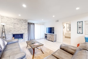 A modern living room with a stone wall, leather sofas, a coffee table, a flat-screen TV, and a fireplace. - Dreamy Desert Hideaway | Pool, Hot Tub & 2 Patios - Near Dining, Shops & Golf (Palm Desert)