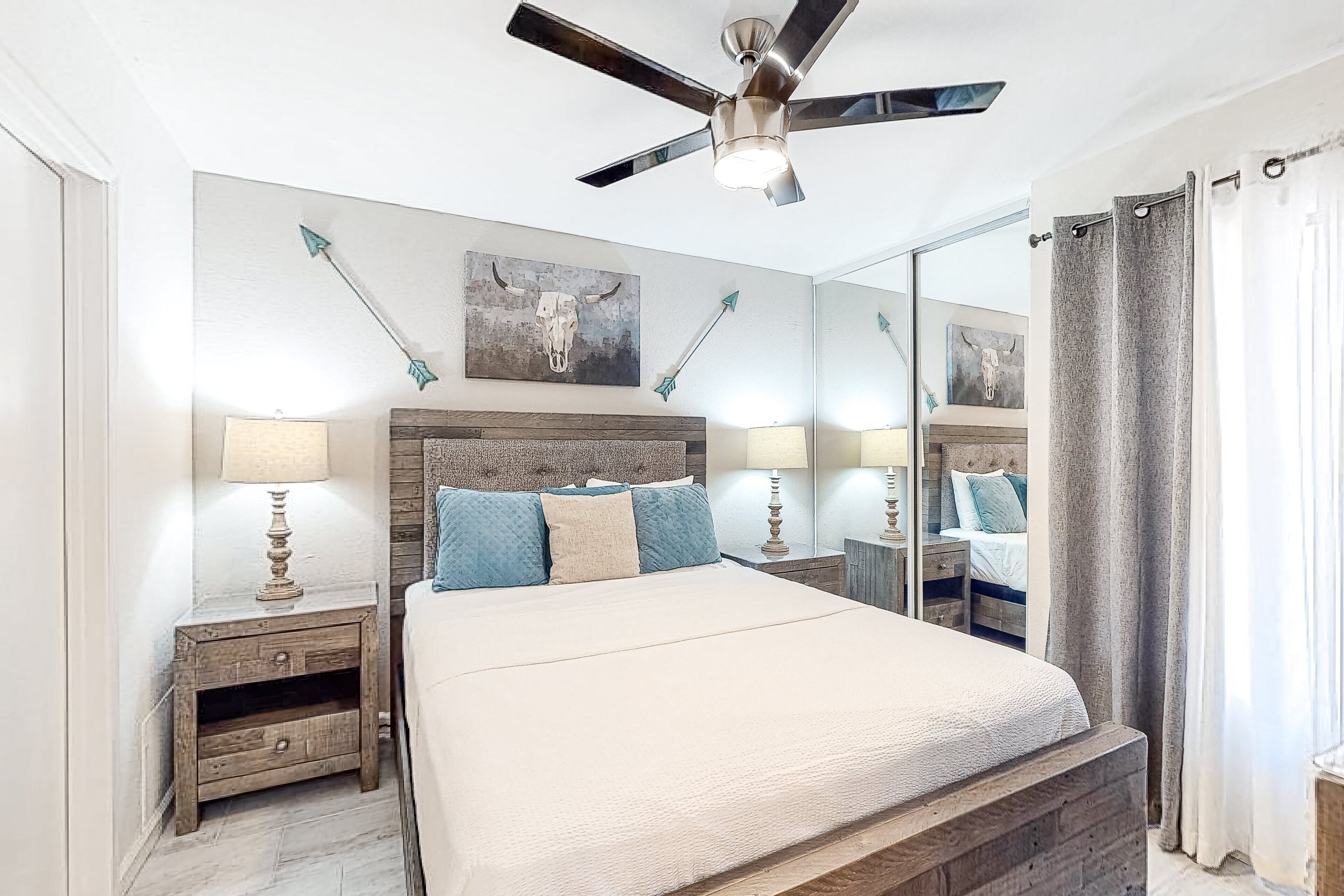 Une chambre à coucher avec un grand lit, une tête de lit en bois, deux tables de chevet avec des lampes, un ventilateur de plafond et un grand miroir.