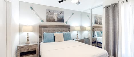 Une chambre à coucher avec un grand lit, une tête de lit en bois, deux tables de chevet avec des lampes, un ventilateur de plafond et un grand miroir.