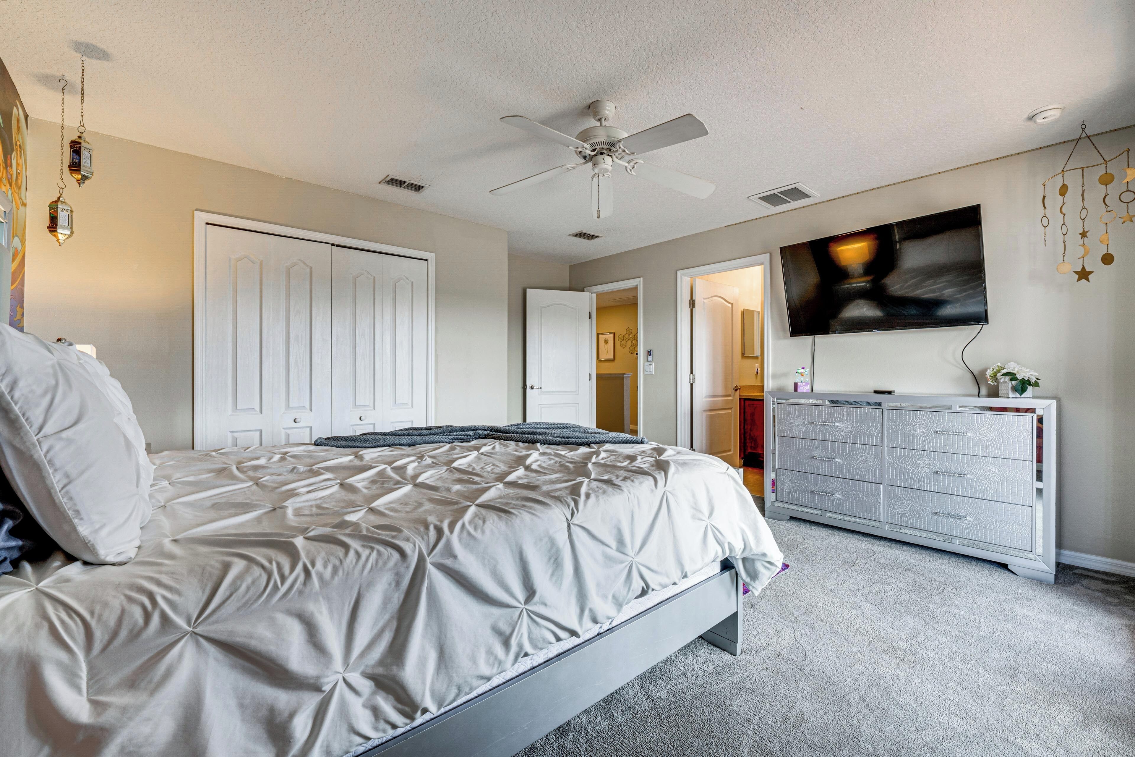 Een slaapkamer met een bed, een dressoir, een plafondventilator en een televisie aan de muur.