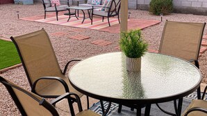 Un'area patio con un tavolino rotondo in vetro, due sedie, una poltrona e un piccolo vaso con una pianta.