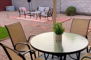Eine Terrasse mit einem runden Glastisch, zwei Stühlen, einer Couch und einem kleinen Blumentopf.
